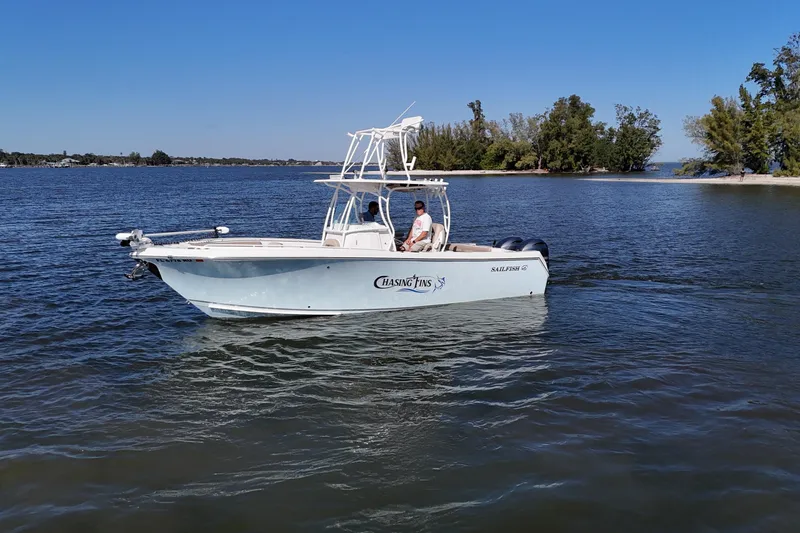 Slide: The Image of 2018 Sailfish 270 CC boat cruising on a calm lake near a wooded shoreline. - 15