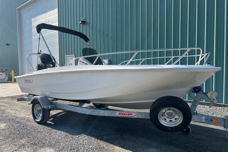 Slide: The Image of 2026 Boston Whaler 160 Super Sport boat on trailer, parked outdoors near a large building. - 4