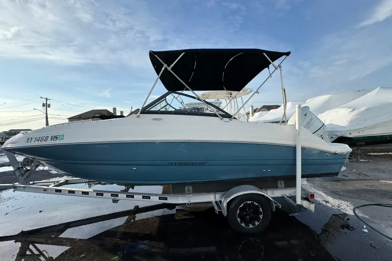 Slide: The Image of 2021 Stingray 201 DC boat on trailer with blue and white hull, black canopy. - 2