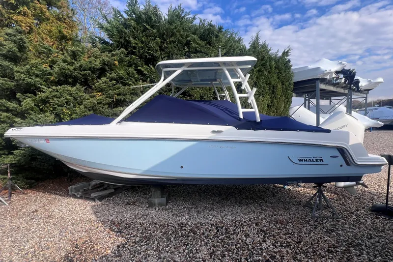 Slide: The Image of 2020 Boston Whaler 230 Vantage boat on display, covered and elevated, surrounded by greenery. - 2