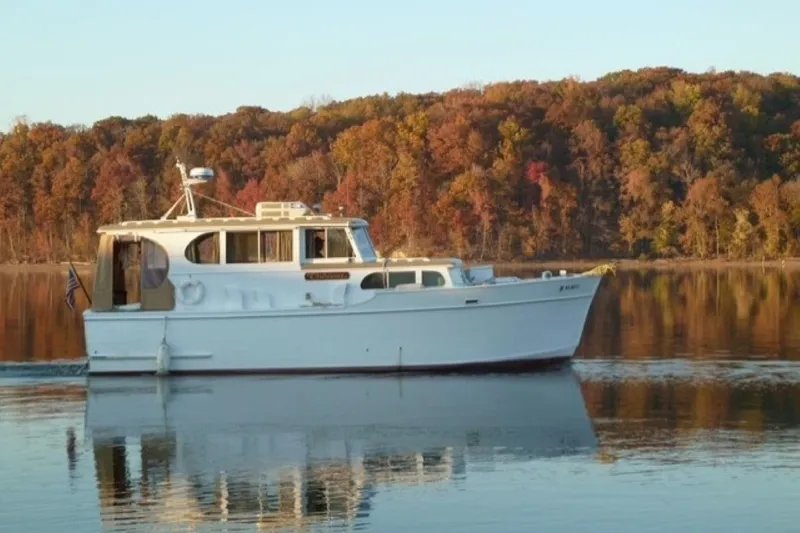 The Image of Custom Cedar Craft 1987 boat cruising on a calm lake with autumn foliage background. - 1