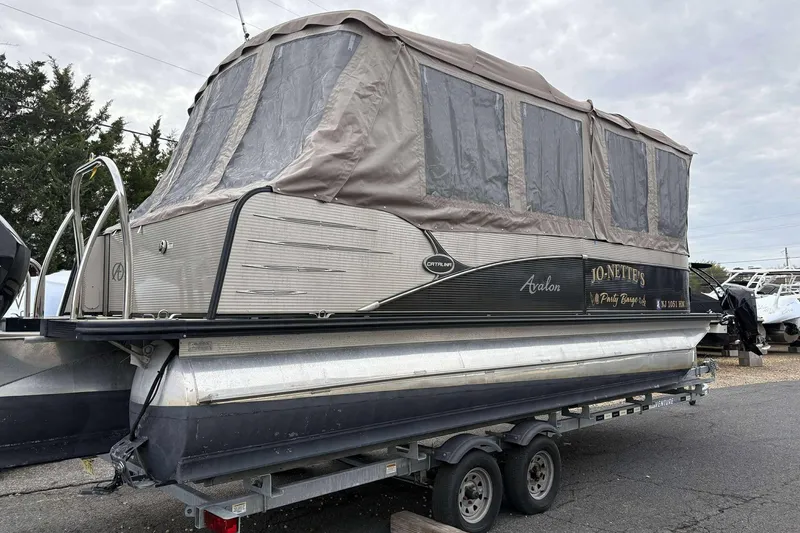 Slide: The Image of 2018 Avalon 2385 EL pontoon boat with canopy on a trailer, parked outdoors. - 25