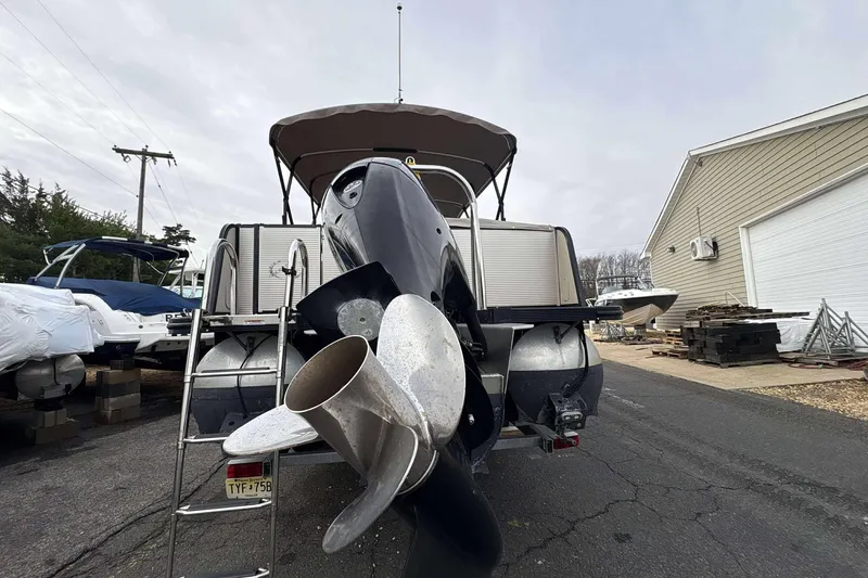 Slide: The Image of 2018 Avalon 2385 EL boat with outboard motor and propeller, parked near a garage. - 6