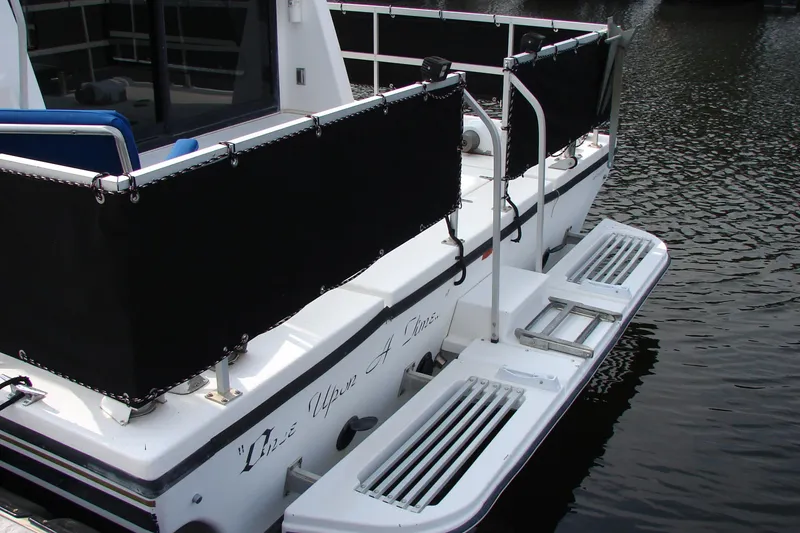 Slide: The Image of 1997 Gibson 47 Sport Houseboat rear view with black rail covers on water. - 40