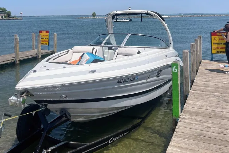 Slide: The Image of 2023 Crownline 280 SS boat docked at a lakeside pier on a sunny day. - 2