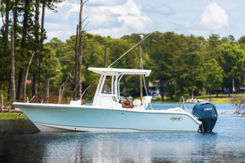Slide: The Image of 2025 Sea Hunt Ultra 229 boat on water, with marina and boats in background. - 2