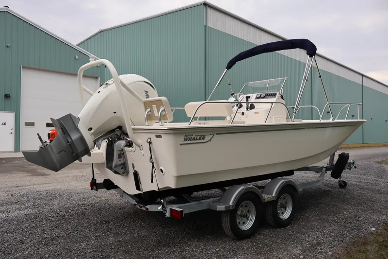 Slide: The Image of 2026 Boston Whaler 190 Montauk boat on trailer, parked near green warehouse. - 5
