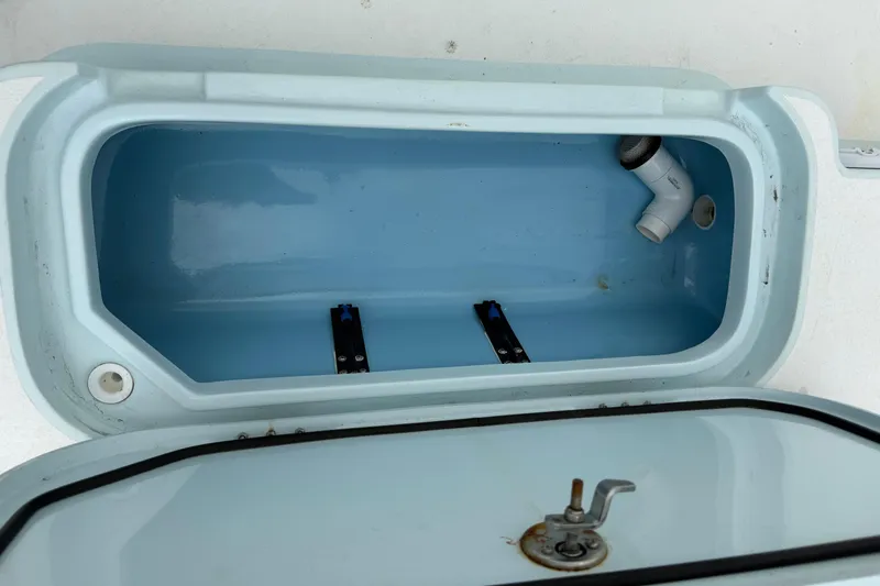 Slide: The Image of Open storage compartment in 2023 Shallow Sport 25 X3 boat, featuring a blue interior and drainage pipe. - 38