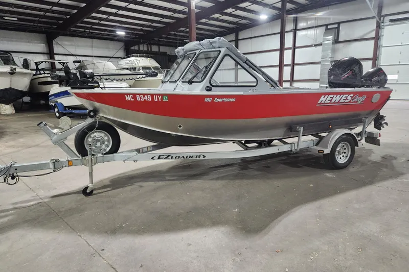 The Image of 2024 Hewescraft 180 Sportsman boat on trailer in indoor storage facility. - 1