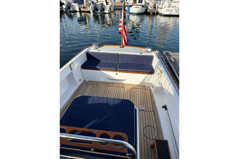 Slide: The Image of 2008 Wasque 26 boat interior with wooden deck and blue seating at a marina. - 20