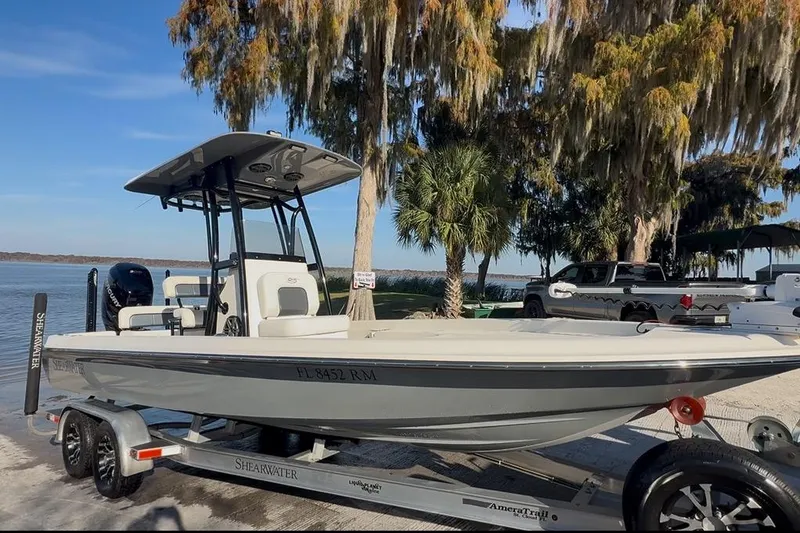 Slide: The Image of 2018 ShearWater 23LTZ boat on trailer by lake, surrounded by trees and parked vehicles. - 1