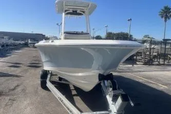 Slide: The Image of 2024 Boston Whaler 220 Dauntless boat on trailer, parked outdoors under clear blue sky. - 2