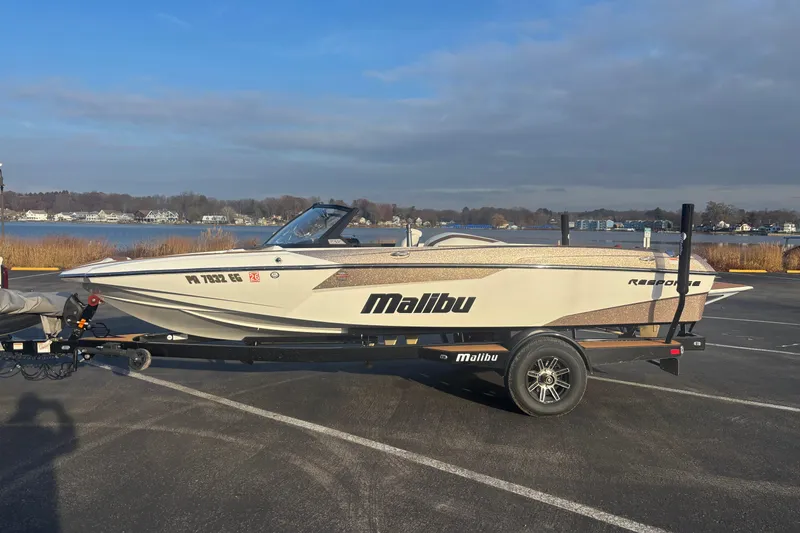 The Image of 2025 Malibu Response TXi boat on trailer by a lakeside parking area. - 0