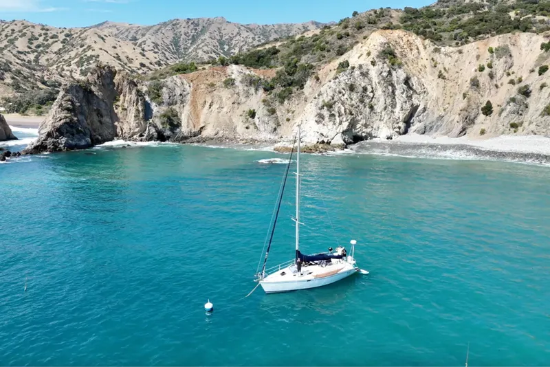 Slide: The Image of Sailboat Catalina 320 (2000) anchored in a scenic coastal bay with rocky cliffs. - 28