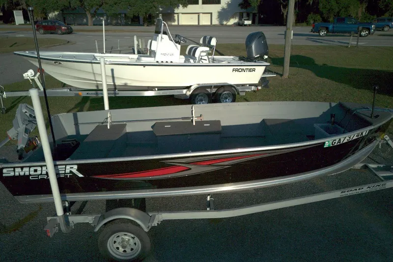Slide: The Image of 2021 Smoker Craft 14 Big Fish boat on trailer, parked beside a white Frontier boat. - 2