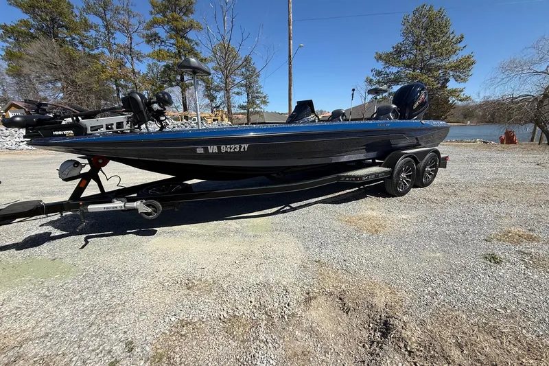 The Image of 2023 Skeeter ZXR21 boat on trailer, parked near a lake with trees in the background. - 1