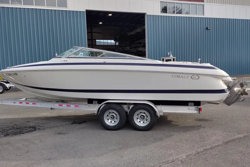 The Image of 2000 Cobalt 246 boat on trailer, parked outside a blue building. - 1