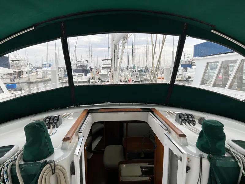 Slide: The Image of Cockpit view of 2004 Beneteau 473 sailboat in marina, featuring green canopy and moored boats. - 18