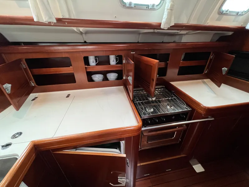Slide: The Image of 2004 Beneteau 473 yacht kitchen with wooden cabinets, stove, and white countertops. - 47