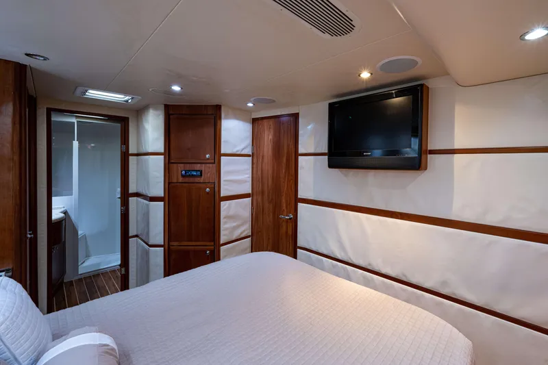 Slide: The Image of Luxurious 2008 Bertram 570 yacht bedroom with TV, wood accents, and ensuite bathroom. - 56