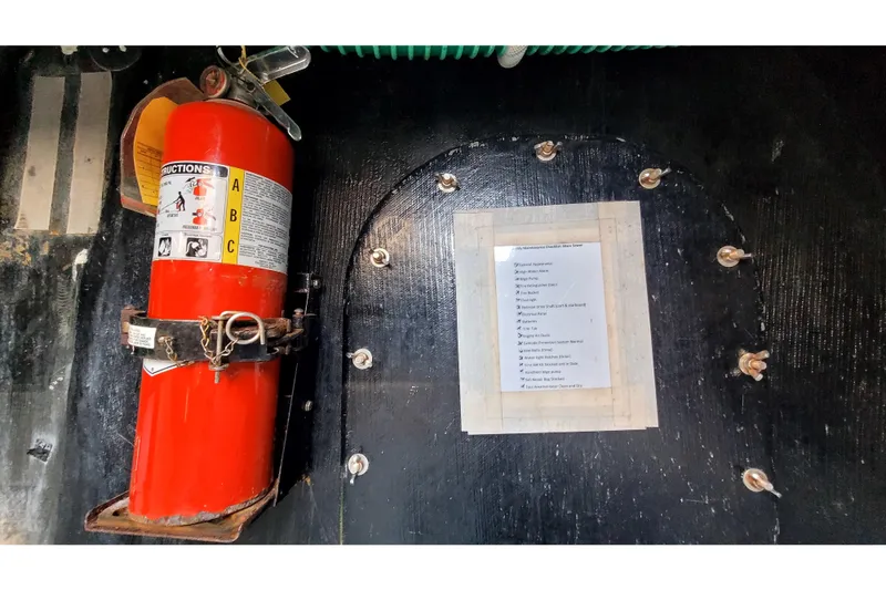 Slide: The Image of Red fire extinguisher and maintenance checklist inside 2002 Custom International Americas Cup Class boat. - 61