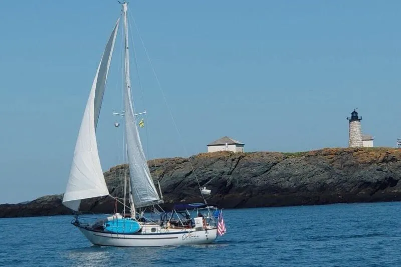 The Image of 1982 Pacific Seacraft 37 sailboat cruising near rocky shoreline with lighthouse. - 0