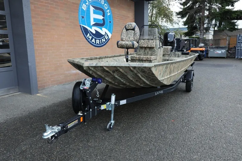 Slide: The Image of 2026 Lund 1870 Predator CC boat with camouflage design on a trailer outside dealership. - 26