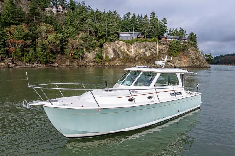 Slide: The Image of 2008 Back Cove 33 boat cruising near rocky shoreline with lush trees. - 11