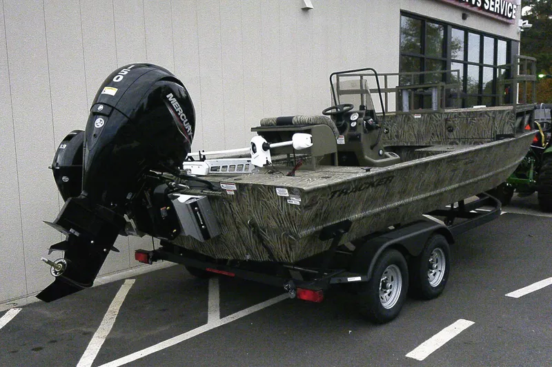 Slide: The Image of 2026 Tracker Grizzly 2072 CC Sportsman Kicker boat on trailer, parked outside a building. - 2