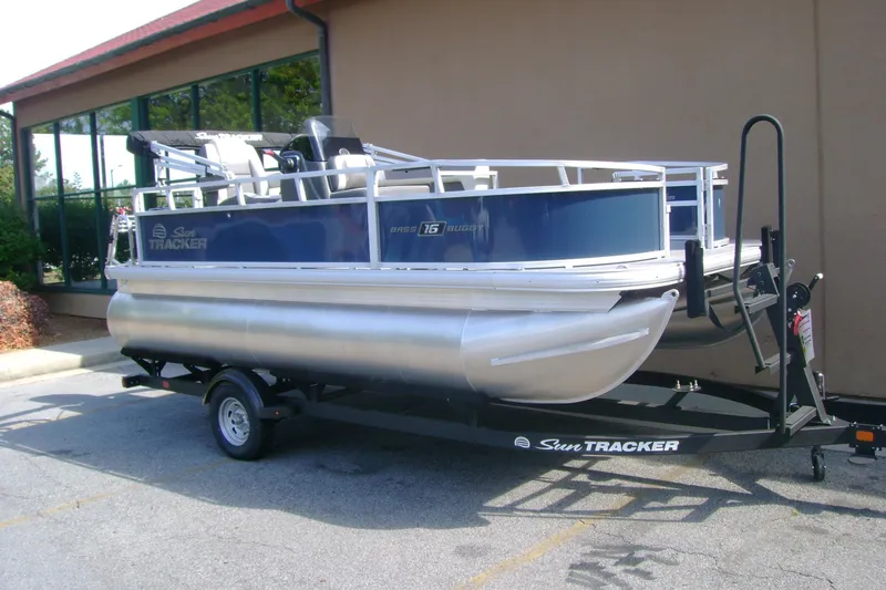 Slide: The Image of 2026 Sun Tracker Bass Buggy 16 XL Select pontoon boat on trailer, parked outdoors. - 1