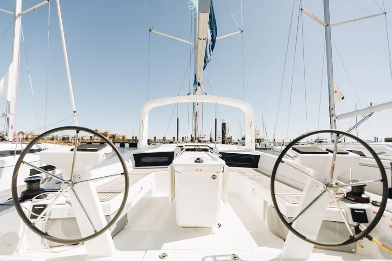 Slide: The Image of 2024 Beneteau Oceanis 46.1 sailboat cockpit with dual steering wheels, docked in marina. - 2