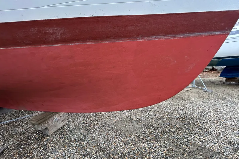 Slide: The Image of Red hull of a 1973 Willard 30 boat on gravel, supported by wooden blocks. - 21