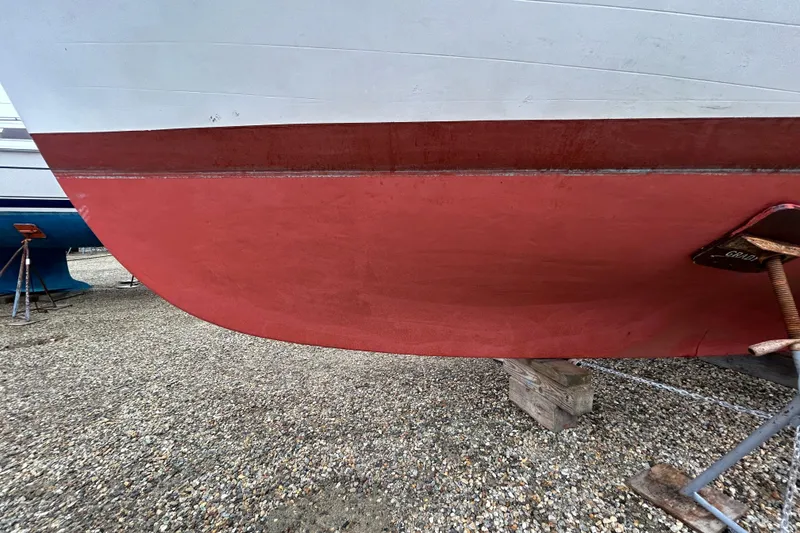 Slide: The Image of Red and white hull of a 1973 Willard 30 boat on gravel. - 25