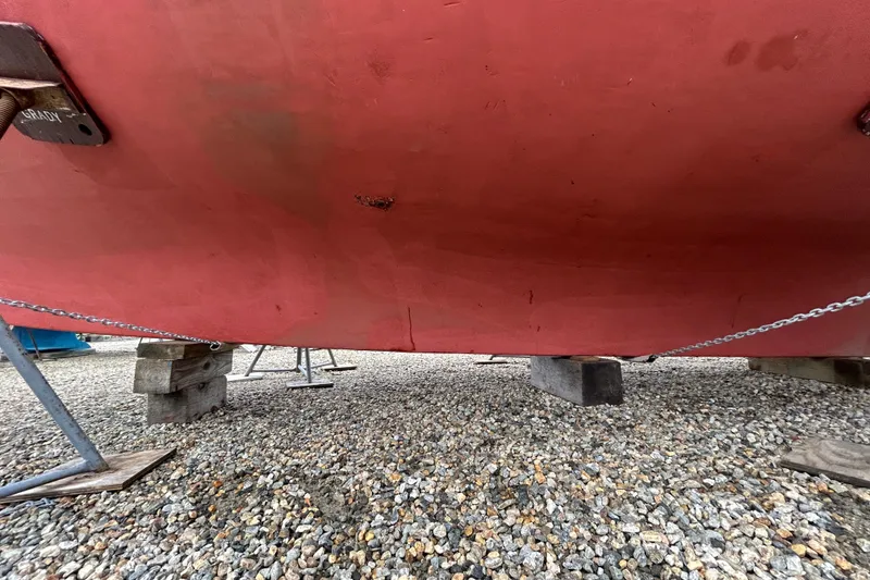 Slide: The Image of Red hull of a 1973 Willard 30 boat on gravel, supported by blocks and chains. - 26