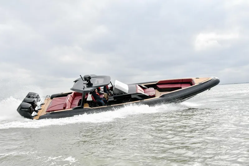 Slide: The Image of 2023 Revolt Comfort 47 boat cruising on water with red seating and dual engines. - 0