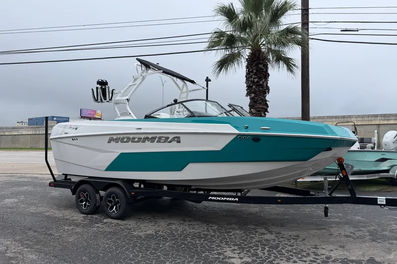 The Image of 2026 Moomba Max boat on trailer, teal and white design, parked near palm tree. - 0