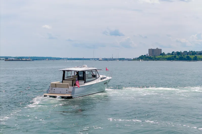 Slide: The Image of 2025 MJM 42 boat cruising on a scenic waterfront with distant cityscape. - 9