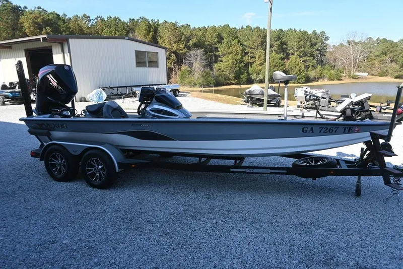 The Image of 2023 Vexus AVX2080 boat on trailer, parked near a lake with trees in background. - 1