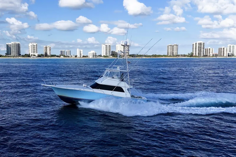 Slide: The Image of 1998 Viking 50 Convertible yacht cruising near coastal city skyline. - 2