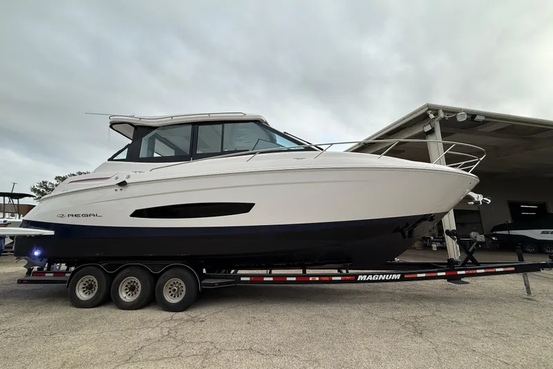 The Image of 2026 Regal 36 Grande Coupe boat on trailer, side view under cloudy sky. - 0