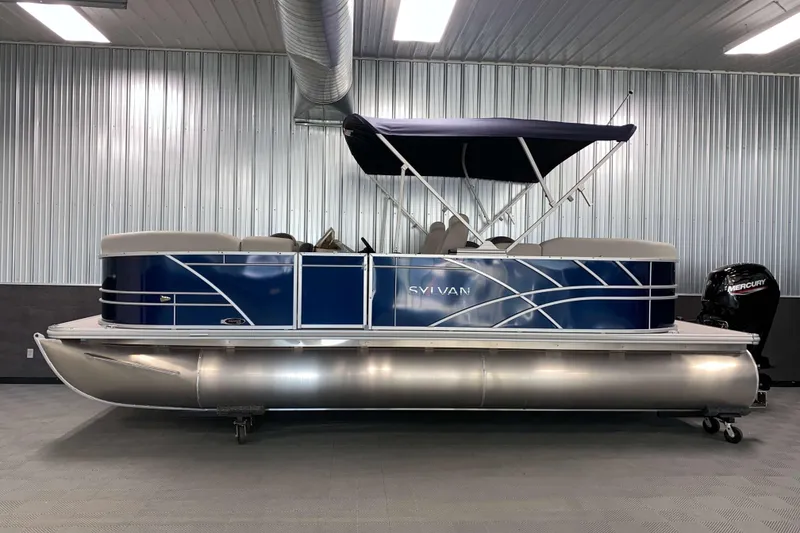 Slide: The Image of 2026 Sylvan Mirage 8522 LZ pontoon boat in showroom, featuring blue exterior and canopy. - 17