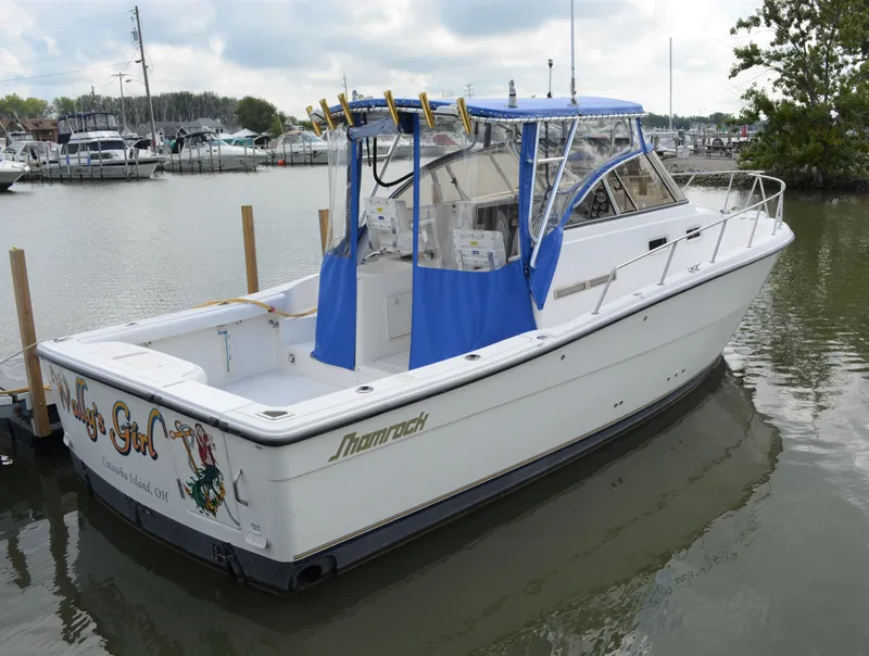 Slide: The Image of 2001 Shamrock 290 Walkaround boat docked, featuring blue canopy and fishing rod holders. - 8