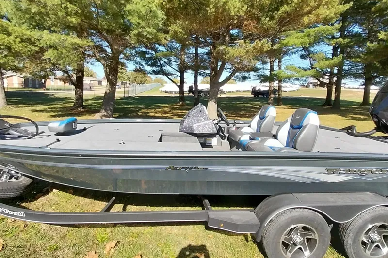 Slide: The Image of 2025 Ranger ALPHA 208 boat on trailer, parked under trees in a sunny outdoor setting. - 1