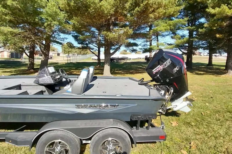 Slide: The Image of 2025 Ranger ALPHA 208 boat on trailer, parked in a grassy area with trees. - 2
