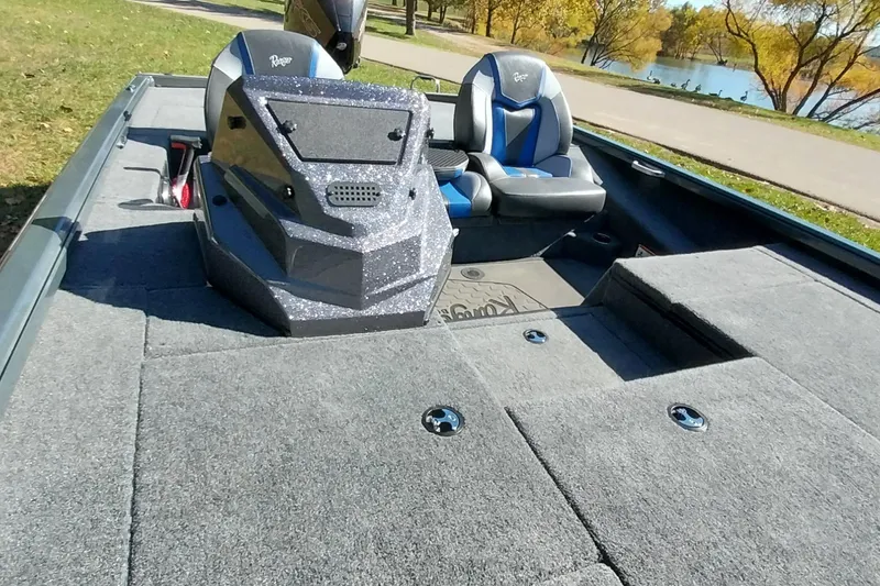 Slide: The Image of 2025 Ranger ALPHA 208 boat interior with gray carpet and blue-accented seats by a lake. - 7
