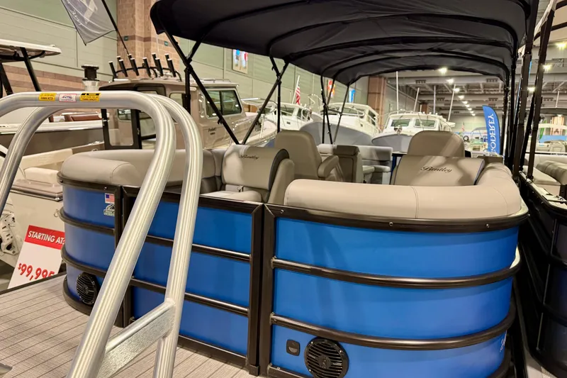 Slide: The Image of 2025 Bentley Pontoons Legacy 243 Navigator, blue exterior, showcased indoors with seating and canopy. - 2