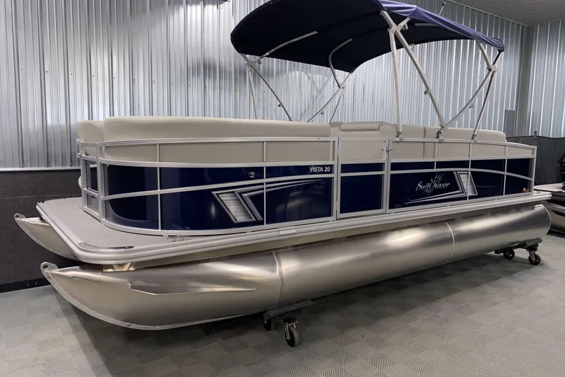 Slide: The Image of 2025 SunChaser Vista 20 CRB pontoon boat with blue and white design in a showroom. - 13