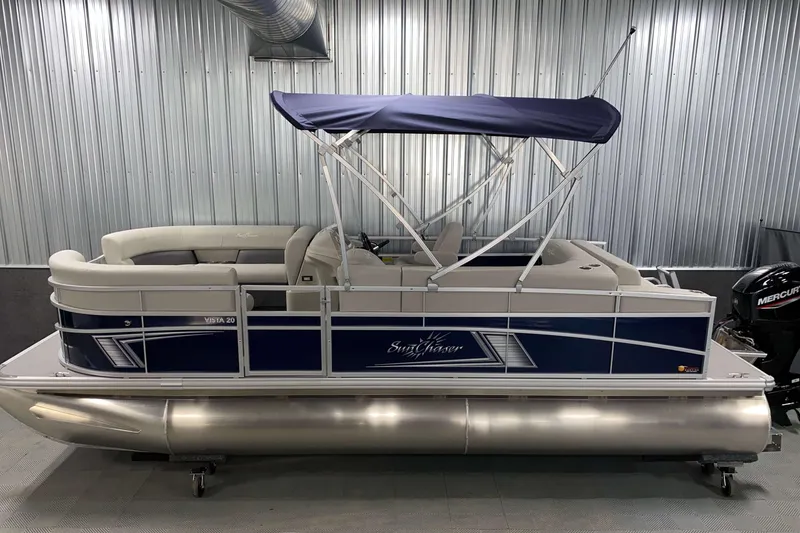 Slide: The Image of 2025 SunChaser Vista 20 CRB pontoon boat with blue canopy in a metal-walled showroom. - 16