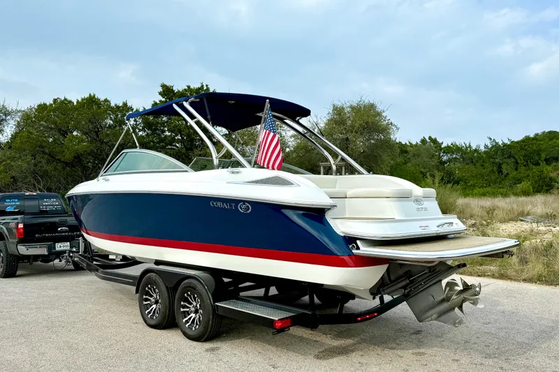 Slide: The Image of 2006 Cobalt 272 boat on trailer with American flag, parked outdoors. - 13
