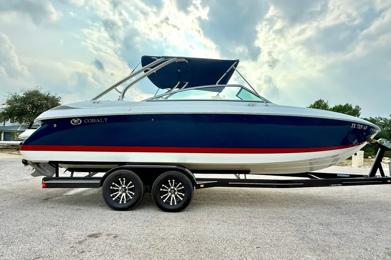 Slide: The Image of 2006 Cobalt 272 boat on trailer, blue and white with red stripe, under cloudy sky. - 17
